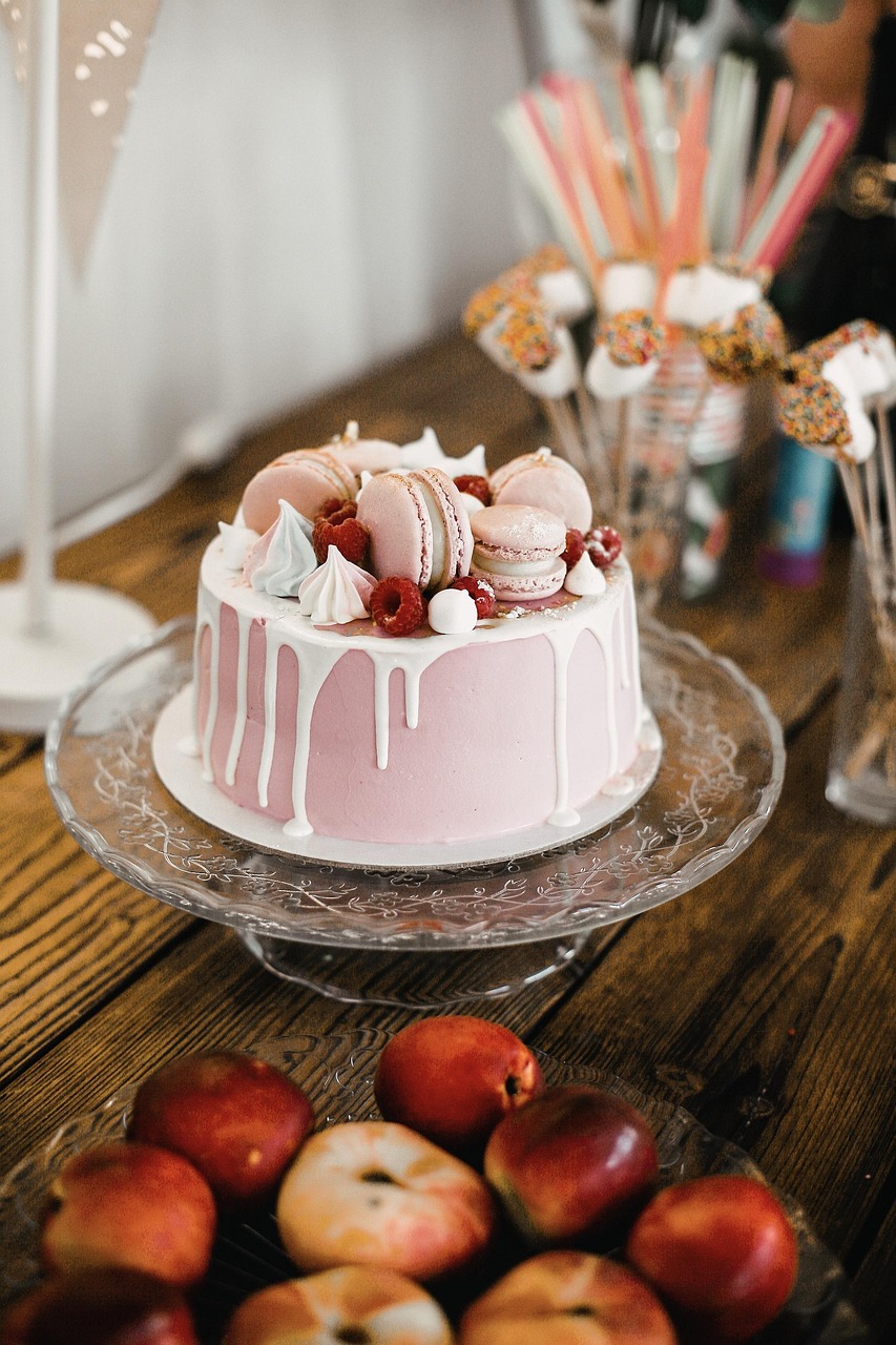 Pink drip celebration cake topped with macarons and meringues on a glass stand